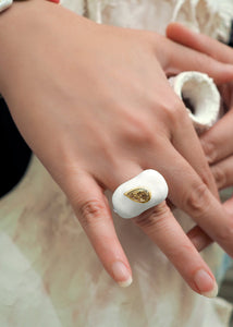 An elegant hand wearing a white color Pear-shape-cut Diamond Square Enamel Ring by www.jingyayi.com.  White textured artistic organic sculptures in the background.